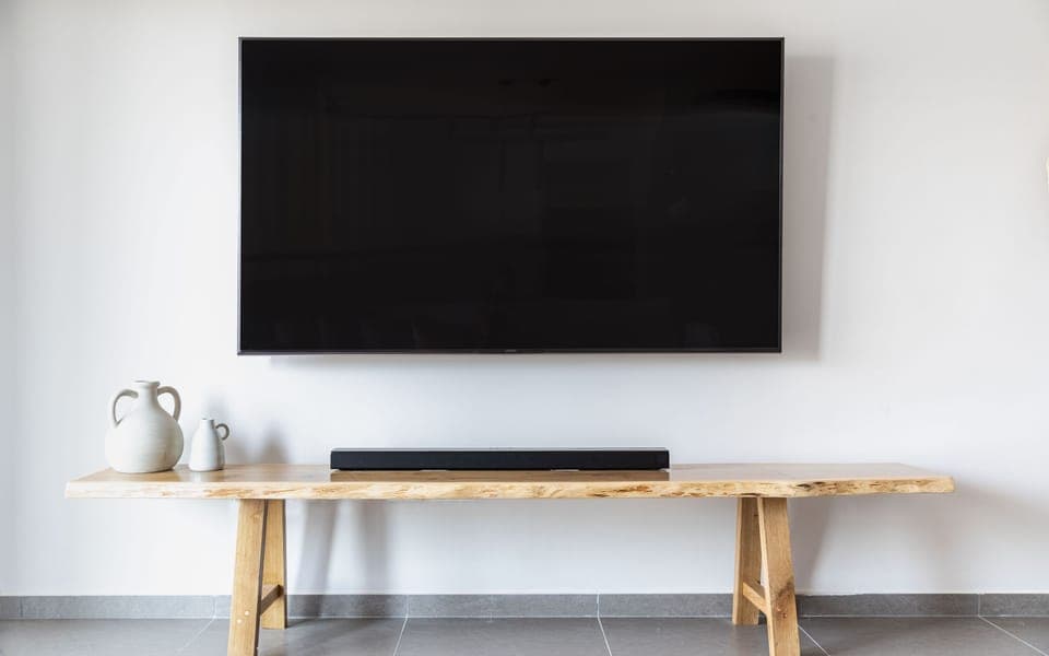 Large TV mounted on a white wall above a wooden console